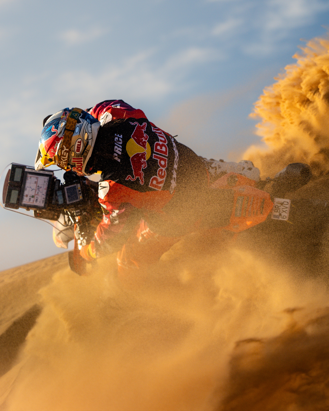 Toby Price riding a dirt bike through sand with a Red Bull branded helmet and Alpinestars enduro gear.