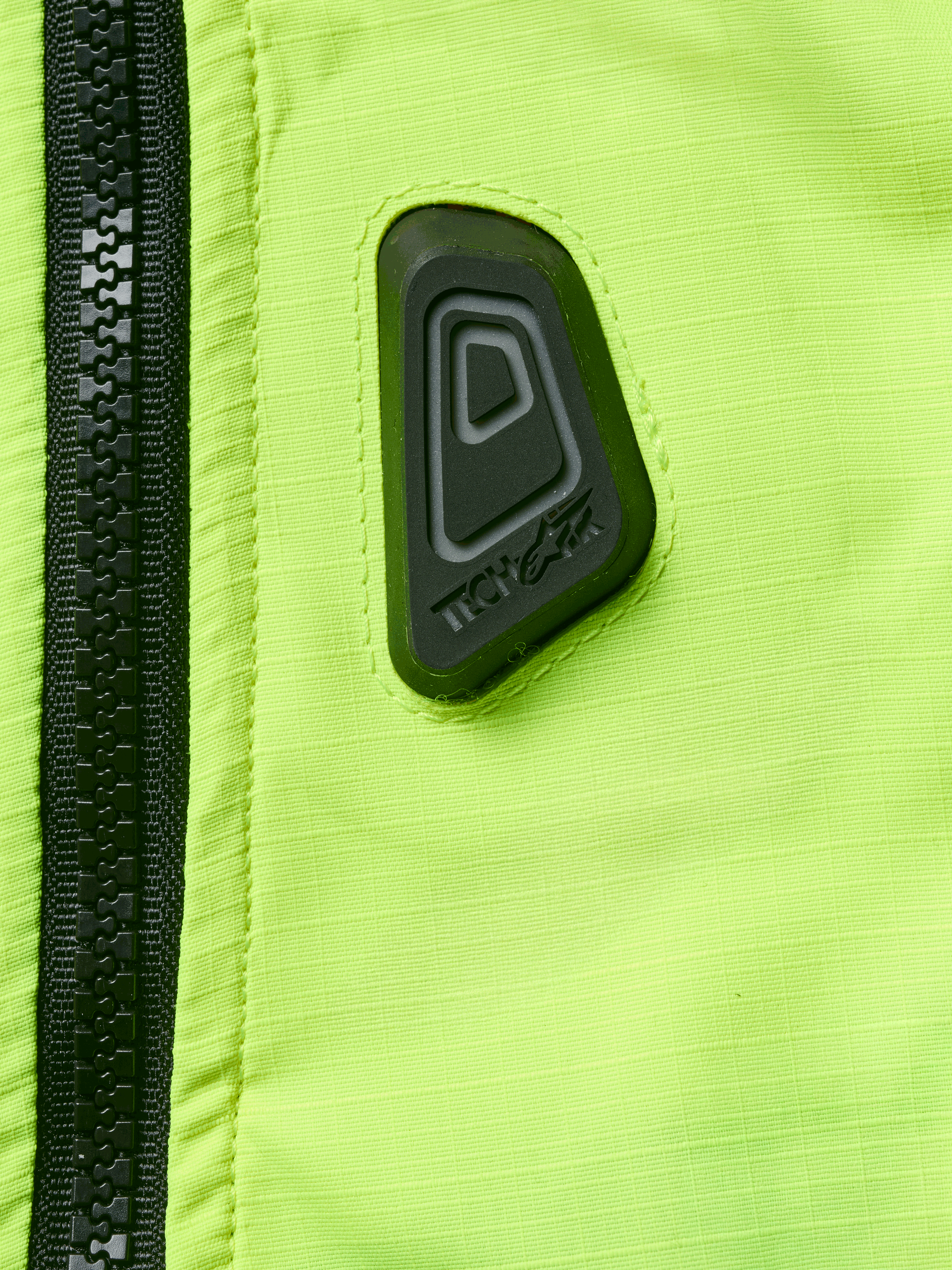 Alpinestars Tech-Air® 3 V2 System, gilet airbag da moto, primo piano del tessuto giallo fluo resistente all'acqua con cerniera nera, con patch gommata nera del logo Tech-Air, dispositivo di sicurezza ad alta visibilità
