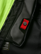Dettaglio del sistema Alpinestars Tech-Air® 3 V2, primo piano della tasca interna in rete con linguetta rossa e chiusura a scatto, pannello giallo fluo vivace, struttura in tessuto nero con etichetta del modulo airbag e cerniera