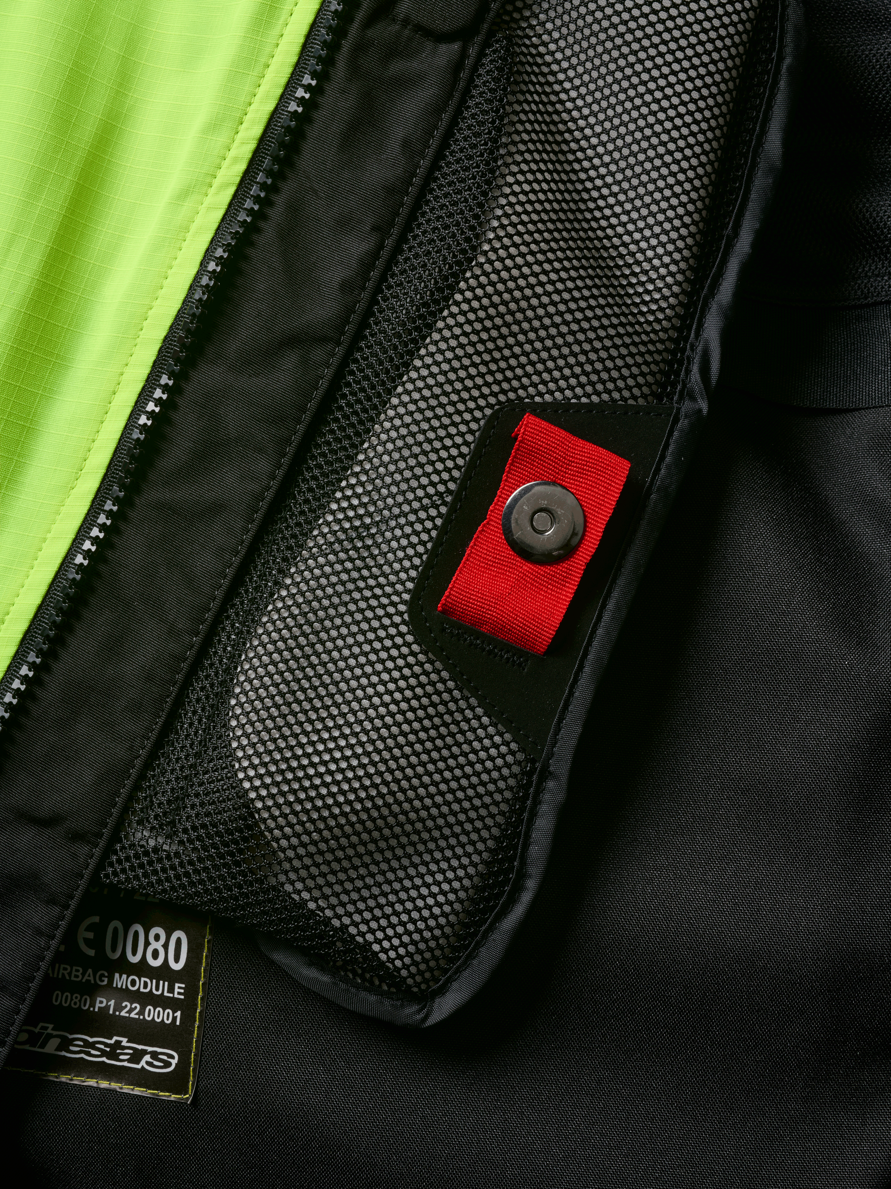 Dettaglio del sistema Alpinestars Tech-Air® 3 V2, primo piano della tasca interna in rete con linguetta rossa e chiusura a scatto, pannello giallo fluo vivace, struttura in tessuto nero con etichetta del modulo airbag e cerniera
