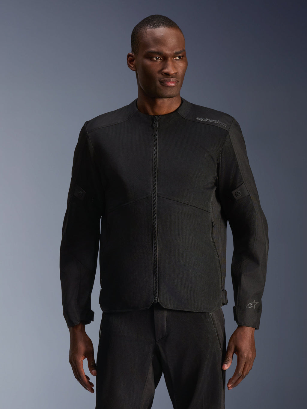 Modello che indossa la giacca Alpinestars C-1 Air in nero, giacca da moto contemporanea con ampi pannelli in rete tecnica e cerniera frontale completa, abbinata a pantaloni da guida neri coordinati, estetica urban lifestyle e per il pendolarismo