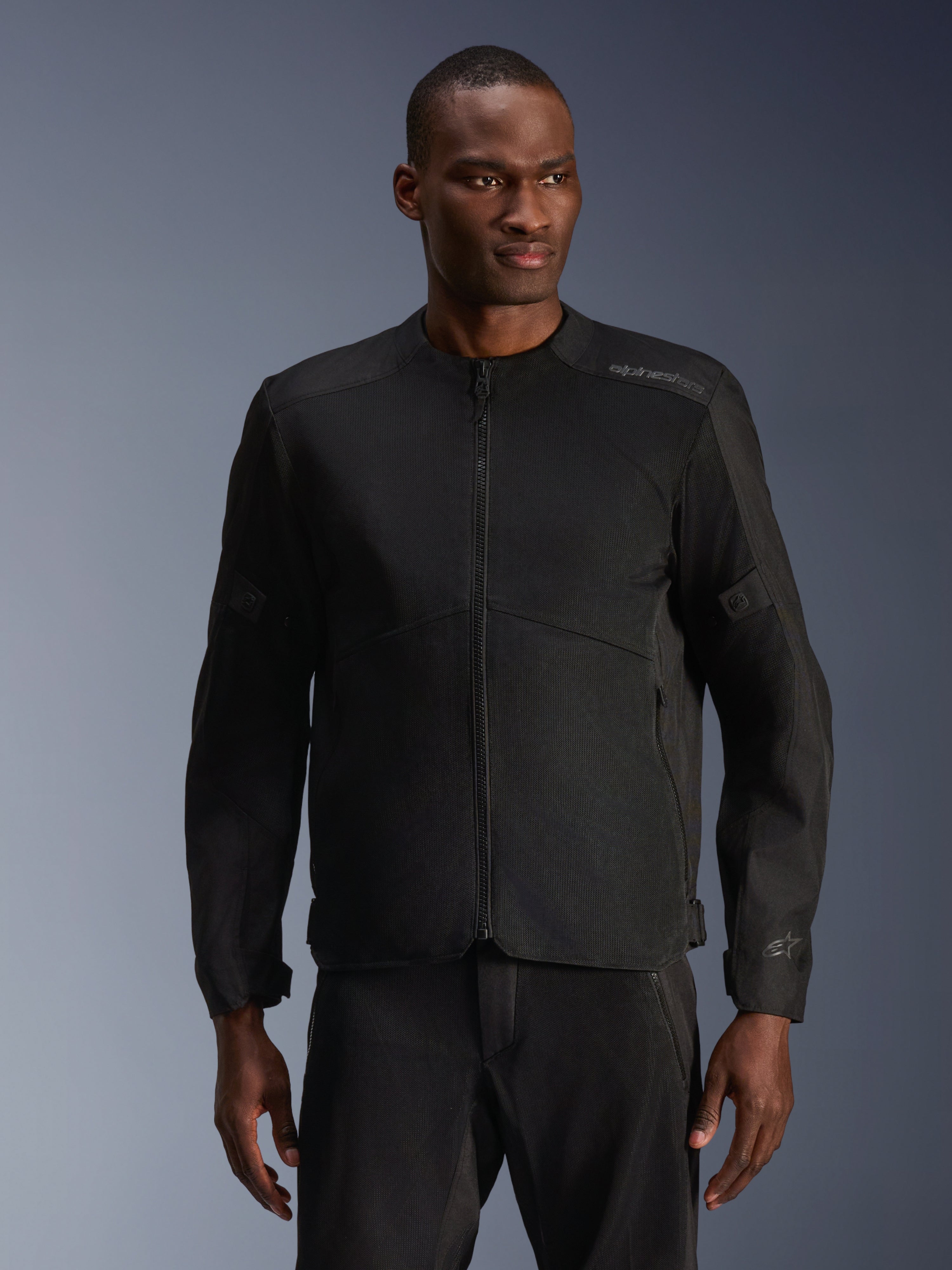 Modello che indossa la giacca Alpinestars C-1 Air in nero, giacca da moto contemporanea con ampi pannelli in rete tecnica e cerniera frontale completa, abbinata a pantaloni da guida neri coordinati, estetica urban lifestyle e per il pendolarismo