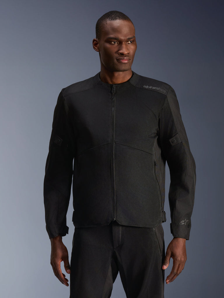 Modello che indossa la giacca Alpinestars C-1 Air in nero, giacca da moto contemporanea con ampi pannelli in rete tecnica e cerniera frontale completa, abbinata a pantaloni da guida neri coordinati, estetica urban lifestyle e per il pendolarismo