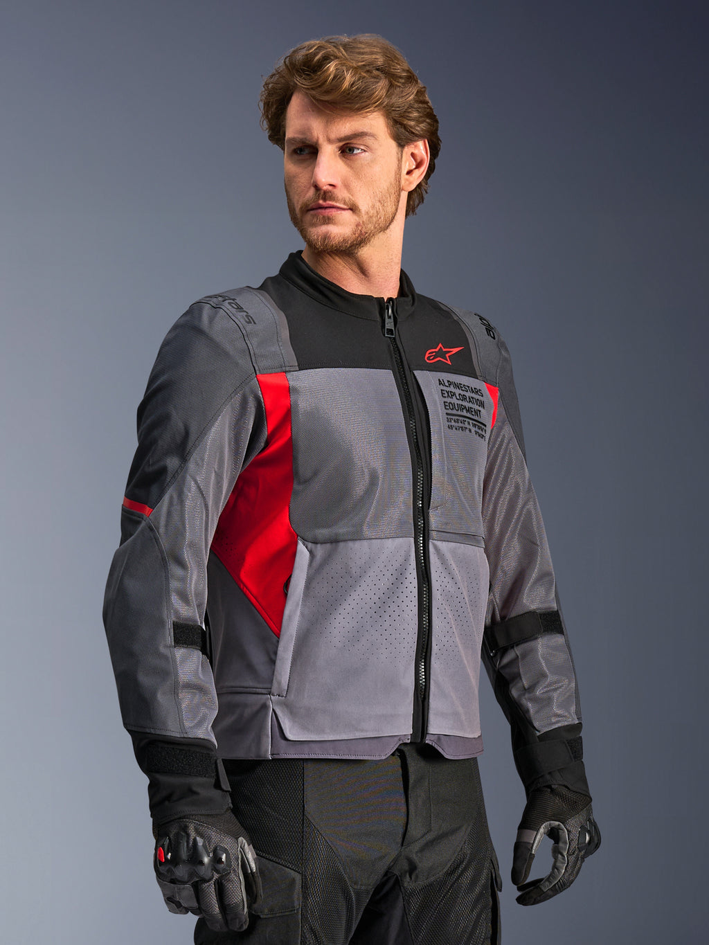 Giacca Alpinestars St-2 Air, giacca da moto, grigio scuro e grigio antracite con dettagli rosso brillante, ampi pannelli di ventilazione in rete, dettagli traforati al laser e logo a stella rosso, indossata da un modello in studio, stile moderno adventure touring
