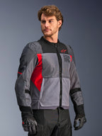 Giacca Alpinestars St-2 Air, giacca da moto, grigio scuro e grigio antracite con dettagli rosso brillante, ampi pannelli di ventilazione in rete, dettagli traforati al laser e logo a stella rosso, indossata da un modello in studio, stile moderno adventure touring