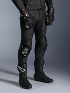 Alpinestars Missile V3, pantaloni da moto racing in pelle nera, indossati con guanti GP Pro e stivali da corsa tecnici, costruzione in pelle premium con saponette per ginocchio con logo bianco, estetica racing professionale per pista e strada