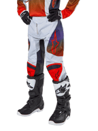 Alpinestars pantaloni Youth Racer Hoen 2024, pantaloni da motocross per ragazzi, grigio chiaro con accenti arancione acceso e nero, con loghi a stella rossi sulle cosce e pannelli rossi sulle ginocchia, indossati con stivali bianchi e neri, design resistente per corse fuoristrada