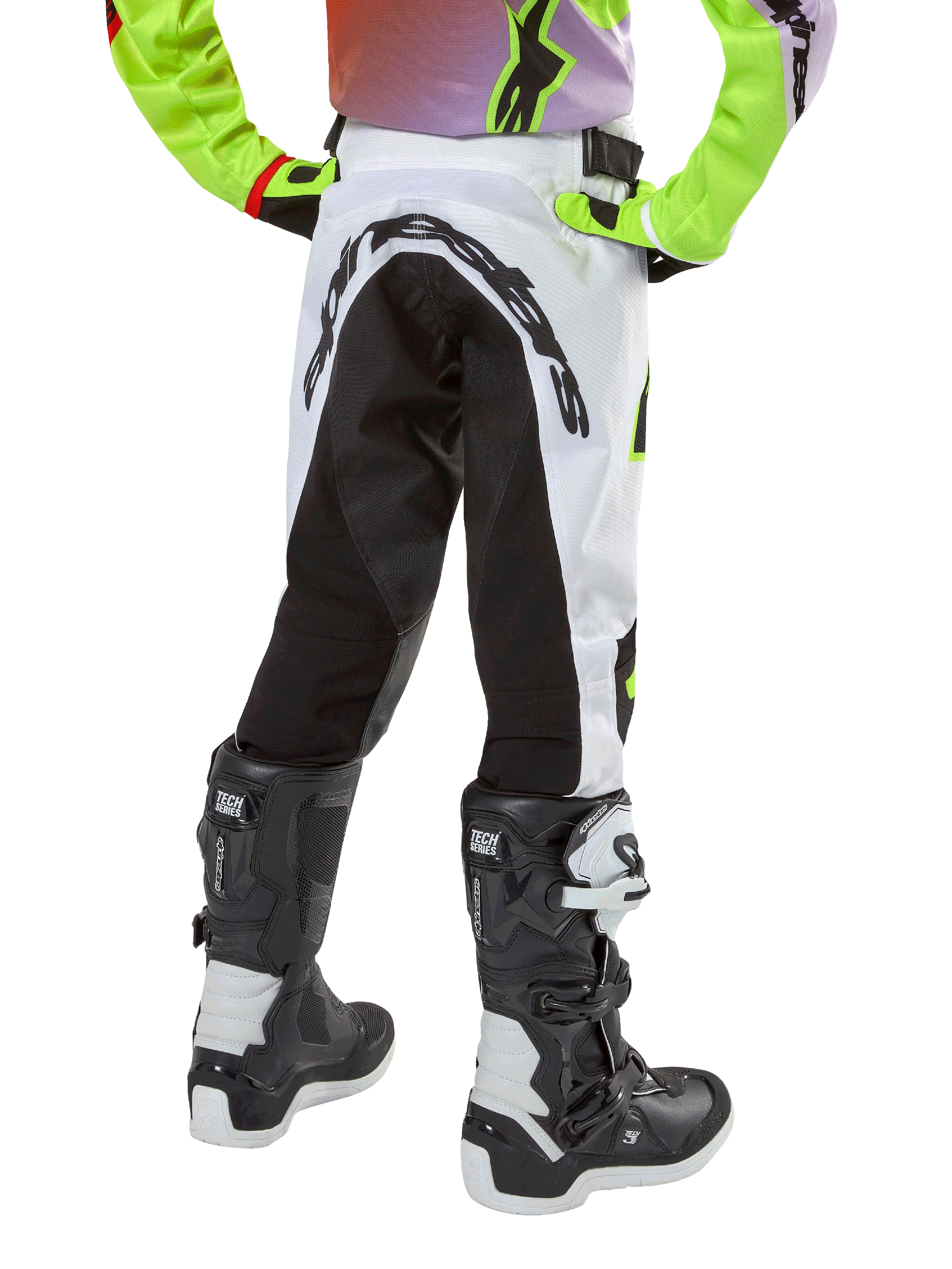 Alpinestars pantaloni Youth Racer Lucent 2024, pantaloni da motocross, bianco e nero con accenti neon, vista posteriore con ampio pannello elasticizzato e logo Alpinestars, indossati con stivali Alpinestars Tech Series bianchi e neri
