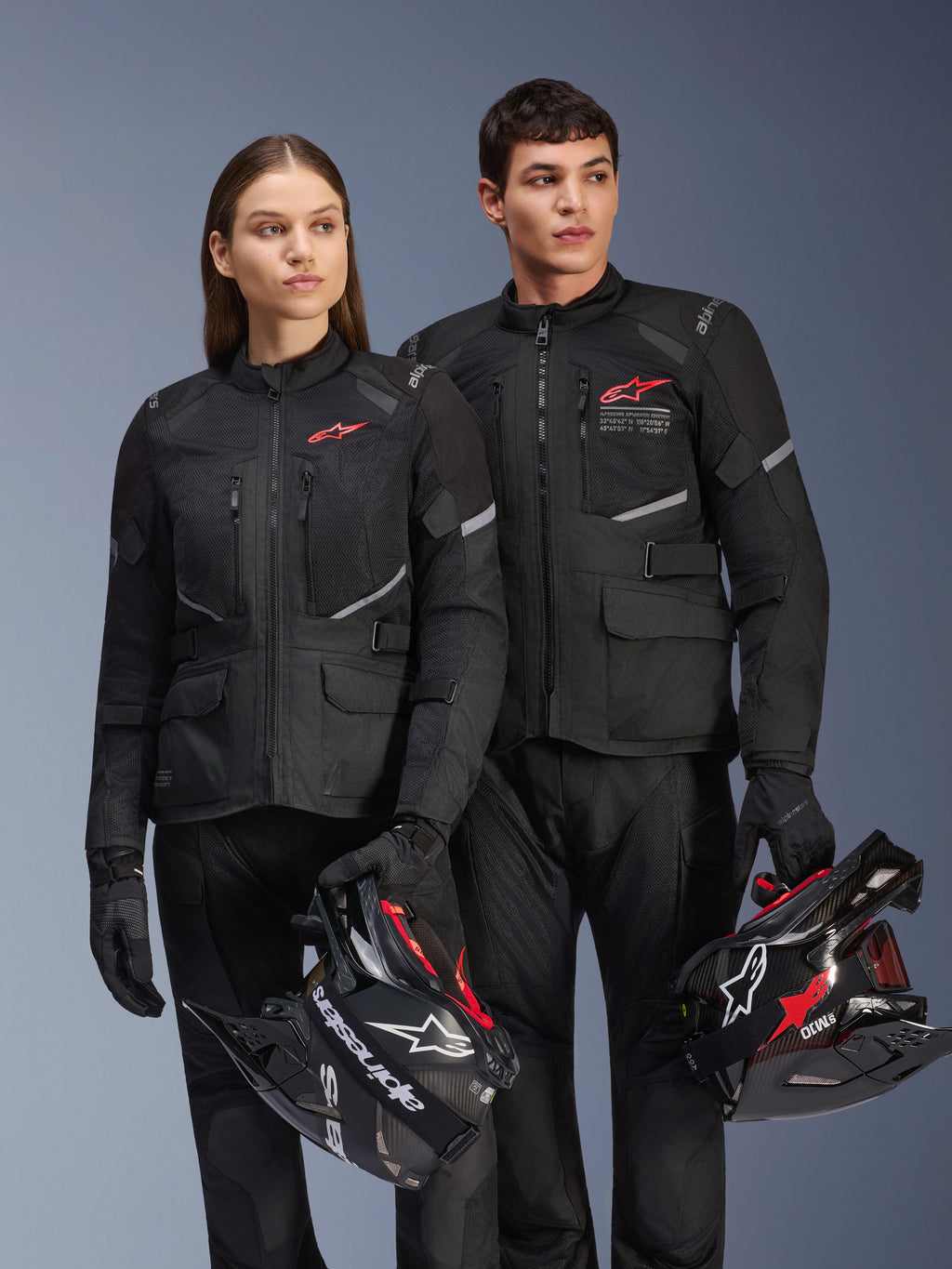 Uomo e donna con giacche Alpinestars Andes Air Drystar®, completo adventure touring nero con pannelli in rete e dettagli riflettenti, pantaloni e guanti neri coordinati, con caschi da motocross, scatto in studio di abbigliamento motociclistico professionale
