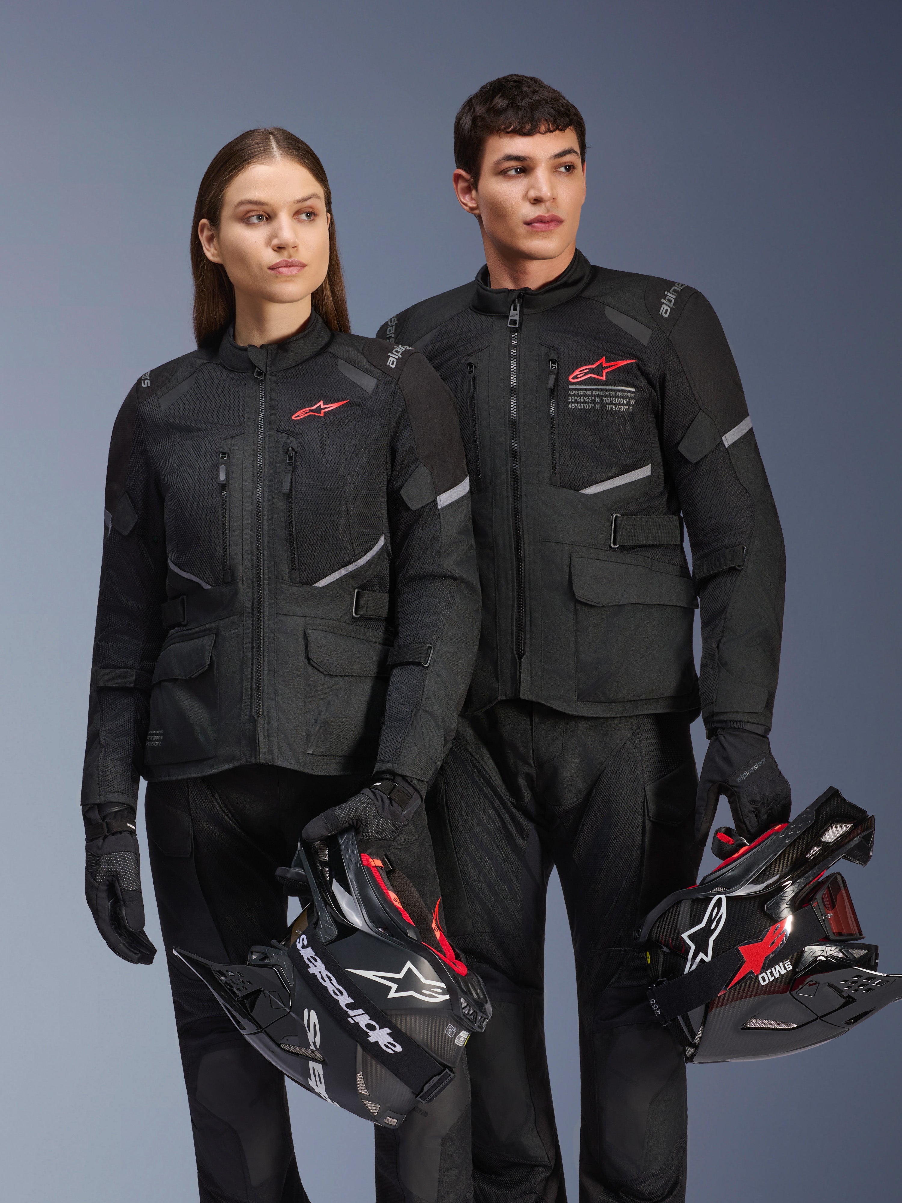 Uomo e donna con giacche Alpinestars Andes Air Drystar®, completo adventure touring nero con pannelli in rete e dettagli riflettenti, pantaloni e guanti neri coordinati, con caschi da motocross, scatto in studio di abbigliamento motociclistico professionale