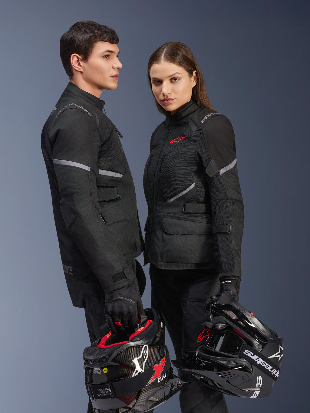 Piloti uomo e donna in abbigliamento da moto Alpinestars, con giacca Stella Andes Air Drystar® in nero, pantaloni e guanti in tessuto coordinati, entrambi con caschi bianchi e neri, scatto in studio di abbigliamento adventure touring coordinato