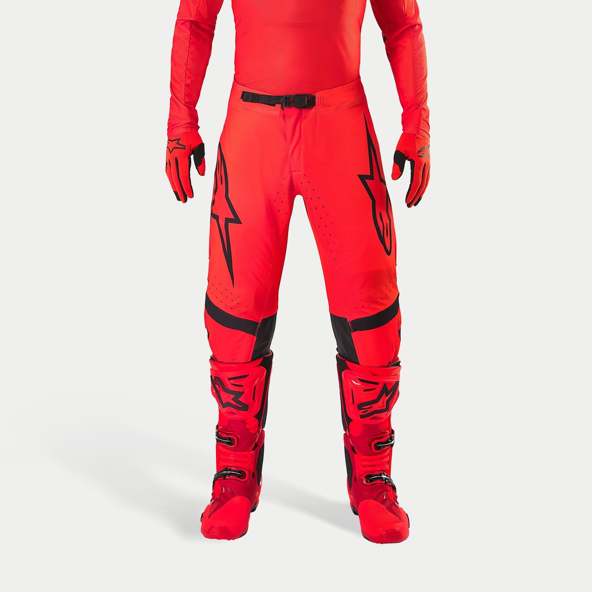 Pantaloni Alpinestars Supertech Ember LE, pantaloni da motocross, rosso fluo e rosso acceso con accenti neri, caratterizzati da vistosi loghi a stella neri sulle cosce, fibbia nera in vita e pannelli sulle ginocchia, indossati con stivali e guanti rossi coordinati per un completo da gara.