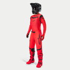 Pilota di motocross con abbigliamento completo da gara, maglia e pantaloni Supertech Ember LE in rosso fluo e nero, casco nero con maschera, stivali e guanti rossi e neri coordinati, completo professionale per corse fuoristrada