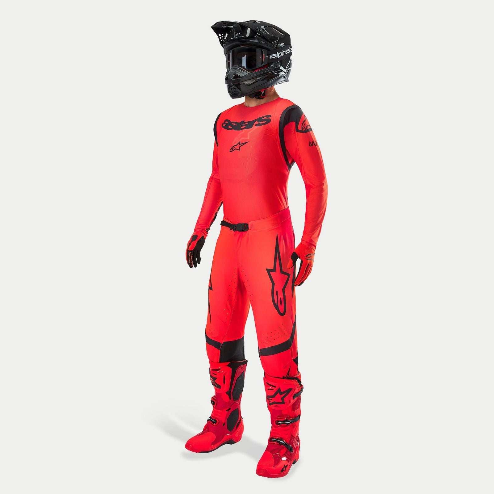 Pilota di motocross con abbigliamento completo da gara, maglia e pantaloni Supertech Ember LE in rosso fluo e nero, casco nero con maschera, stivali e guanti rossi e neri coordinati, completo professionale per corse fuoristrada