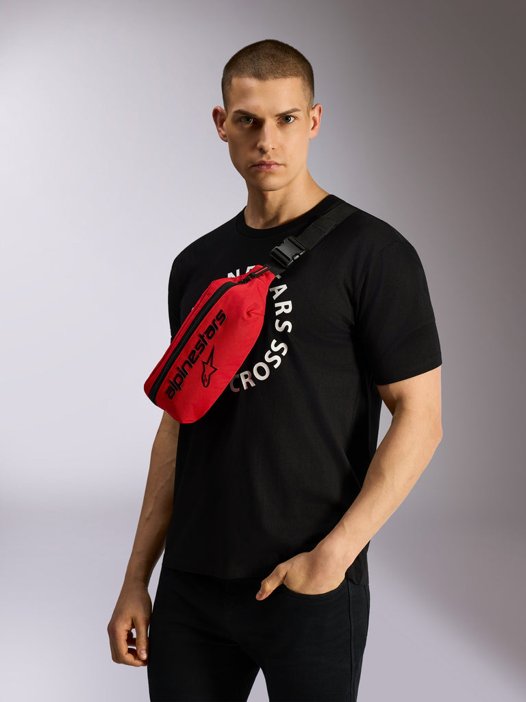 Marsupio Alpinestars Only Linear in rosso e nero, indossato a tracolla su una t-shirt grafica nera, caratterizzato dal logo Alpinestars nero in evidenza e da una cinghia regolabile per un look urban casual